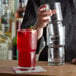 A person pouring a red drink into a Libbey Newton Stackable Beverage Glass on a table.