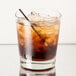 A Libbey Heavy Base English Double Old Fashioned Glass filled with ice and brown liquid with a straw.