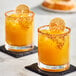 Two glasses of passion fruit drinks with orange slices and lemon garnish.