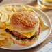 A cheeseburger on a Turano sesame hamburger bun with potato chips on a plate.