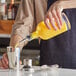 A person holding an Acopa clear glass bottle and pouring a drink into a cup.