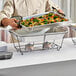 A man in a chef's uniform using a black wire rack for a foil pan of food.