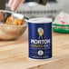 A person holding a blue bowl of Morton Iodized Salt on a kitchen counter.