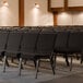 Lancaster Table & Seating silver vein church chairs with black fabric in rows in a room.