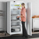 A woman standing in front of a white Galaxy reach-in refrigerator with a closed door.