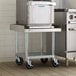 A Regency stainless steel equipment stand with casters holding a large stainless steel oven.