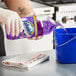 A person in gloves pouring Fabuloso multi-purpose cleaner into a blue bucket.