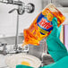 A person in gloves pouring Ajax Triple Action Orange Scent dish soap into a bowl.