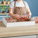 A person holding a white Choice greenhouse tray full of strawberries.