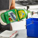 A person pouring Fabuloso Passion Fruit Scent multi-purpose cleaner from a green bottle into a blue container.