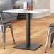 A table with a black steel standard height table base column supporting a marble top.