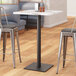 A Lancaster Table & Seating black steel bar height table base with a black pole on a table in a restaurant dining area.