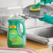 A person in green gloves uses Palmolive Essential Clean dishwashing liquid to clean a pan in a home kitchen sink.
