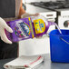 A person in gloves pouring Fabuloso multi-purpose cleaner into a blue bucket.