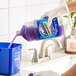 A hand pouring Fabuloso Lavender Scent multi-purpose cleaner into a blue container.