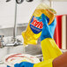 A person in yellow gloves pouring Ajax Ultra lemon dish detergent into a bowl.