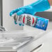 A person in blue gloves spraying Easy-Off Fume-Free Lemon Scent Oven Cleaner on a metal surface.