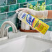 A person in gloves using a yellow Professional Lysol spray bottle to disinfect a sink.