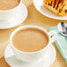 A wooden table with a Twinings Chai Latte in a white cup and a pastry.