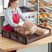 A woman in a red apron places loaves of bread in a Baker's Lane brown bread tray on a bakery display counter.