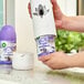 A person holding a white Air Wick refill canister with a purple label and a hole in the top.