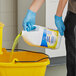 A person in blue gloves pouring yellow Lysol cleaner into a bucket.