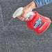 A hand holding a white spray bottle spraying Resolve carpet cleaner on a carpet.