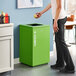 A woman standing next to a Lancaster Table & Seating green steel compost receptacle with open top lid.