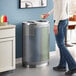 A woman standing next to a Lancaster Table & Seating stainless steel trash can with trash and recycle openings.