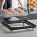 A woman using a black Baker's Lane bread tray dolly to transport bread in plastic bags.