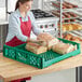 A woman in a red apron and gloves holding a green Baker's Lane bread tray with loaves of bread.