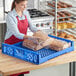 A woman in a red apron using a blue Baker's Lane bread tray to display bread on a counter.