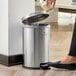 A woman putting a coffee cup in a silver Lancaster Table & Seating stainless steel round step-on trash can.