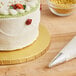 A Baker's Lane gold cake drum on a counter with a frosted cake.