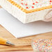 A person using a Baker's Lane white cake drum to cut a cake.