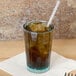 A close-up of a Cambro Azure Blue polycarbonate tumbler filled with brown liquid and ice with a straw in it.