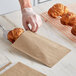 A person in a plastic glove using a pizza cutter to cut a croissant into a customizable kraft bag.