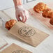 A person putting a croissant in a customizable kraft bag.