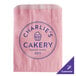 A pink paper bag with blue text that says "Charlie's Bakery"