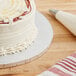 A close-up of a Baker's Lane silver cake drum on a table with a cake and a knife.