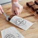 A person in gloves cutting a brownie and putting it in a white paper bag.