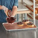 A person pouring Henry & Henry Classic Chocolate Dip Icing on doughnuts.