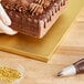 A hand using a knife to cut into a chocolate cake on a gold cake drum.