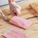A hand using a spatula to put a piece of cake in a customizable pink paper bag.