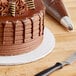 A chocolate cake on a Baker's Lane white cake drum on a table in a bakery display.