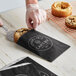 A hand placing a cookie in a black paper bag.