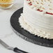 A Baker's Lane black cake drum with a cake on a plate next to a knife.