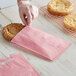 A hand in plastic gloves putting a cookie in a customizable pink paper bag.