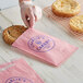 A hand putting a cookie in a customizable pink paper bag.