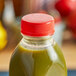 A bottle of green juice with a red tamper-evident cap on a table.